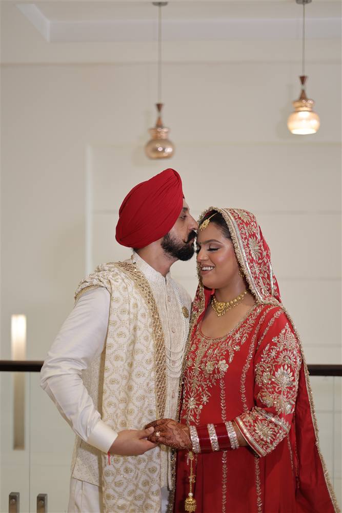 Groom kissing bride forehead red lehenga candid Rattu Studio